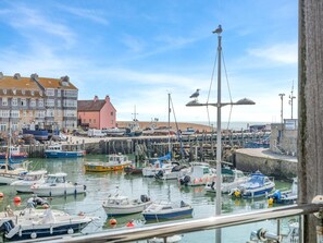 Ein Hafen mit verschiedenen Schiffen an den Kai, eine Möwe auf einer Konstruktion und Gebäude im Hintergrund.