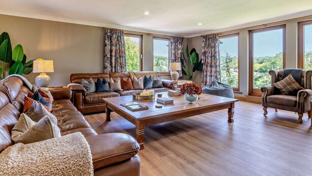 A spacious living room with leather sofas, a coffee table, and large windows offering a view of greenery. - 6 Bed in Perth (oc-96289) (Stanley)