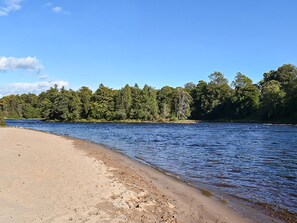 En strand med en flod, träd och klarblå himmel.