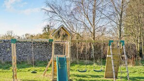 A playground with a wooden climbing structure, a slide, and swings. - 3 Bed in Carnforth (oc-96319) (Yealand Redmayne)