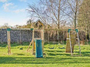 Ein Spielplatz mit einer hölzernen Kletterkonstruktion, einer Rutsche und Schaukeln.