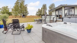 Eine Terrasse mit Whirlpool, Gartenmöbeln und einem überdachten Sitzbereich.