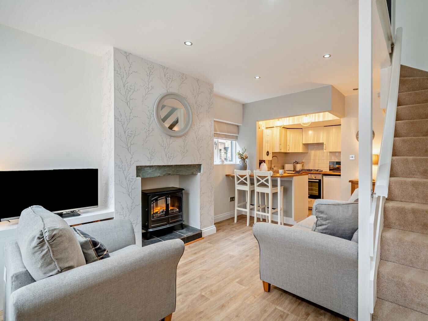 A living room with a fireplace, two sofas, a TV, and a kitchen in the background.