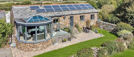 Una casa de piedra con un invernadero de cristal, un techo con paneles solares y un jardín bien cuidado.