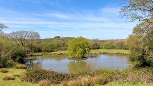 A serene pond surrounded by grassy areas and trees. - 2 Bed in Bude (oc-96290) (Poundstock)