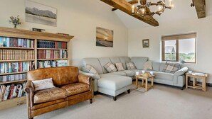 A cozy living room with a leather sofa, a light-colored sectional, a wooden bookshelf, and a chandelier. - 2 Bed in Bude (oc-96290) (Poundstock)