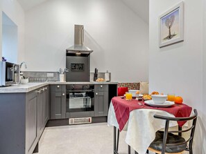 A compact kitchen with grey cabinets, a stainless steel range hood, and a dining area with a red tablecloth. - 1 Bed in Pickering (oc-96309) (Allerston)