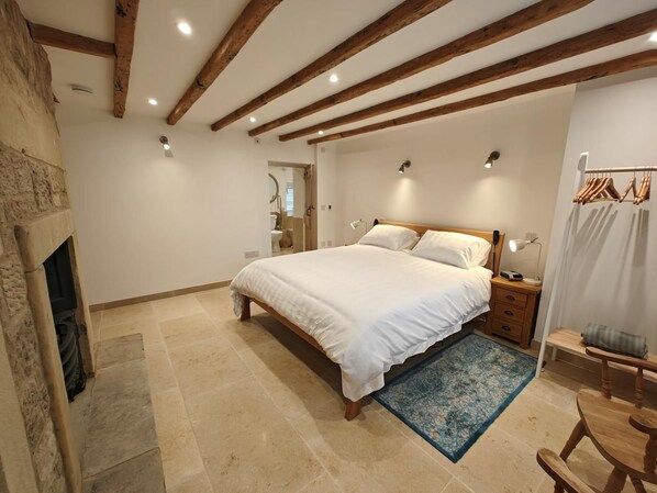 Ein Schlafzimmer mit einem großen Bett, Holzbalken, einem Steinkamin und einem blau gemusterten Teppich.