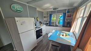 Kompakti keittiö, jossa on jääkaappi, liesi, pesuallas ja ruokapöytä tuoleineen.