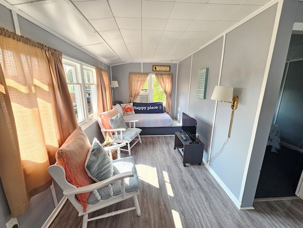 Una habitación con cama, escritorio, silla, lámpara y ventana con cortinas.