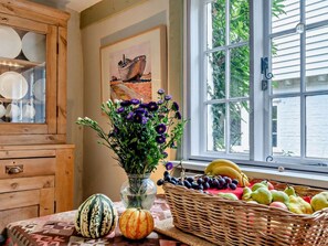 A kitchen with wooden cabinets, a vase with flowers, a fruit basket, and a window with greenery outside.