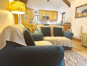 A cozy living room with a sofa, a lamp, and a kitchen in the background. - 2 Bed in Holsworthy (oc-beeba) (Thornbury)
