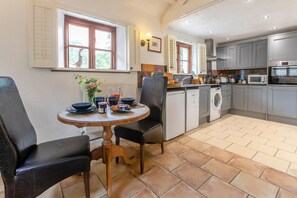 A kitchen with a dining area, including a table with chairs, a washing machine, and a microwave. - 1 Bed in Holsworthy (oc-dairc) (Thornbury)