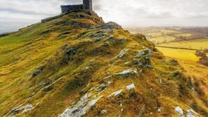 Eine Burg auf einem grasbewachsen Hügel unter blauem Himmel.