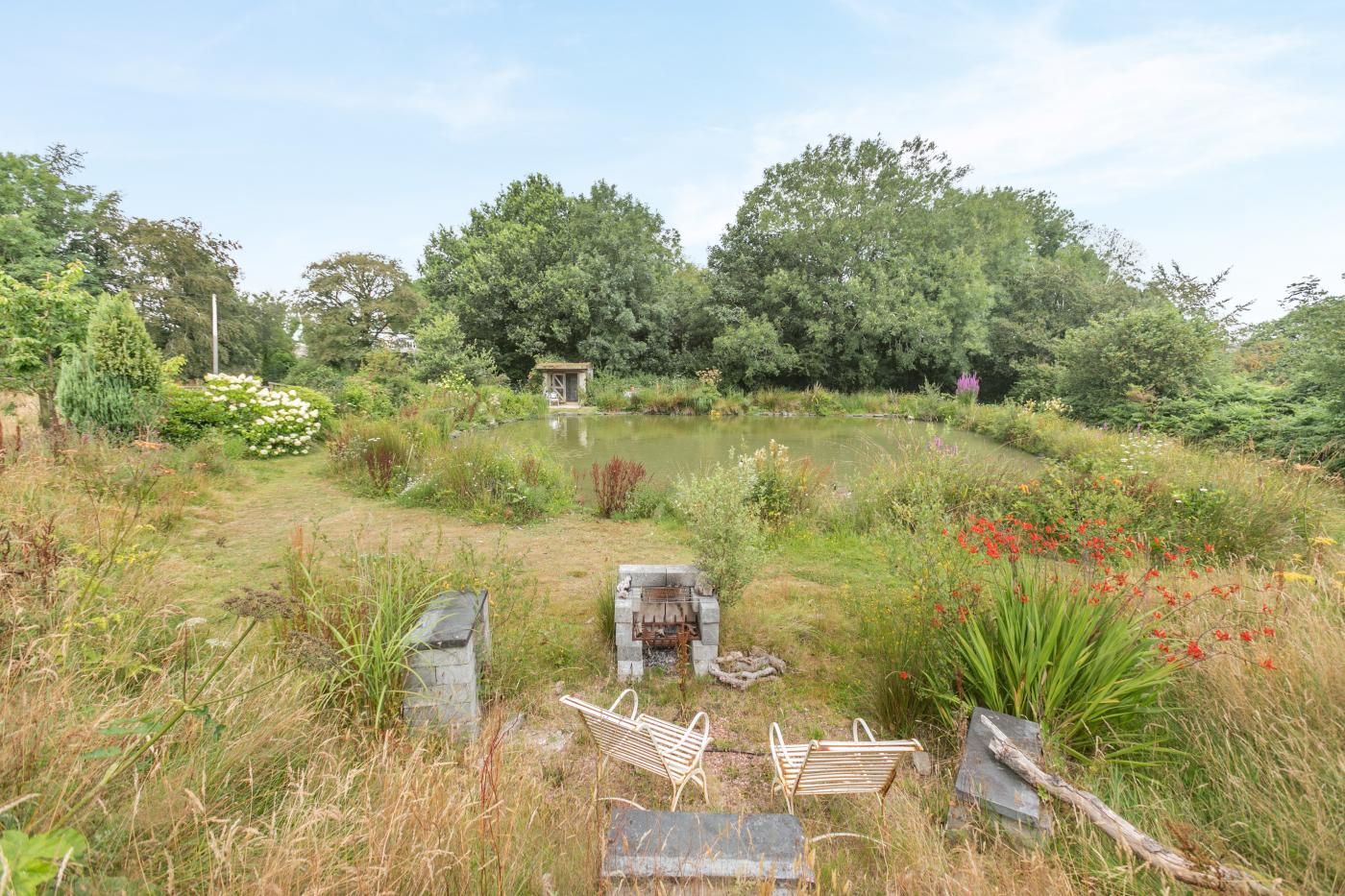 A garden with a pond, wooden benches, and a small structure.