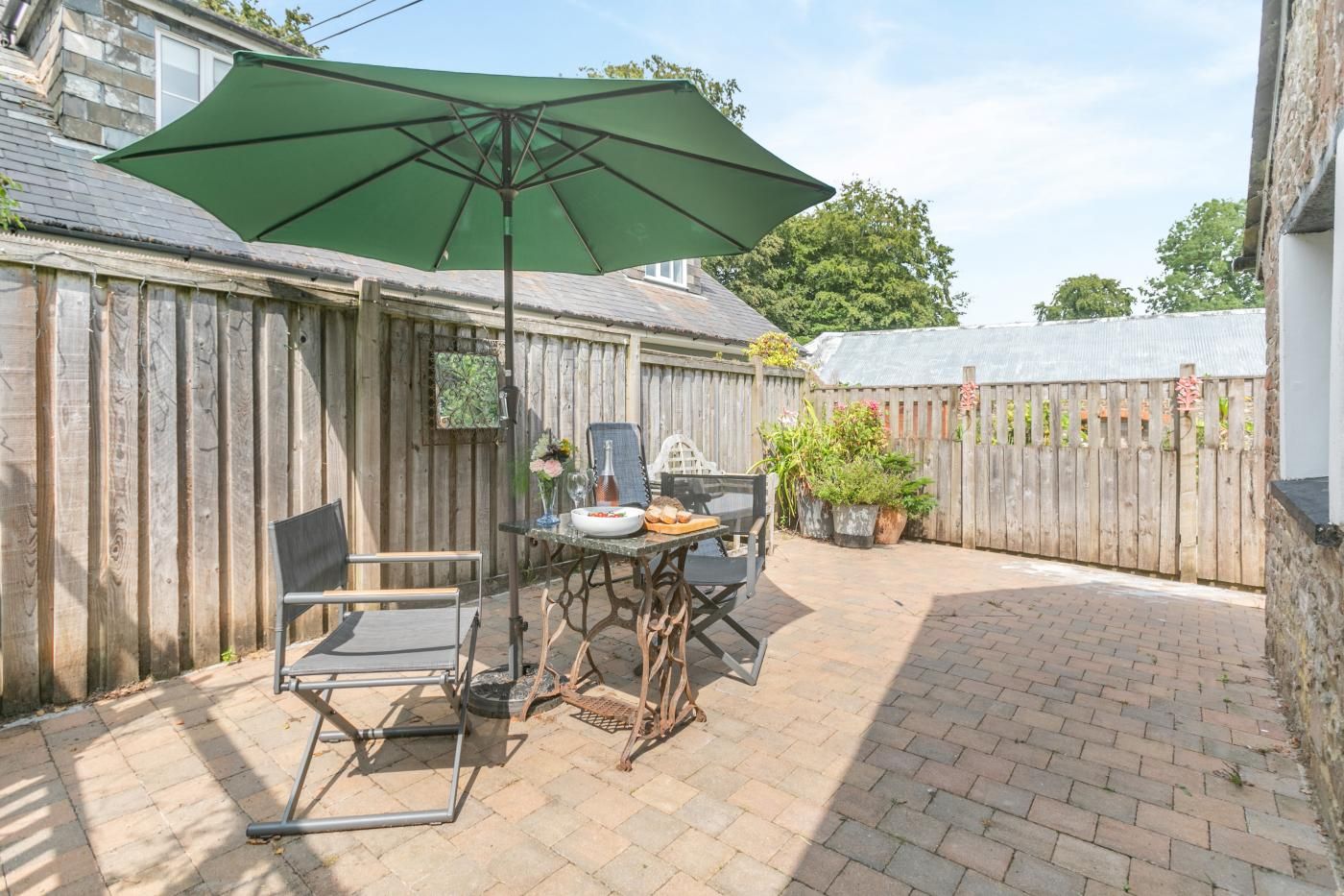 Une terrasse avec une table, des chaises et un parasol vert.