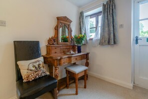 A room with a wooden dresser, a bench, a chair with a decorative pillow, a mirror, and a window with curtains. - 1 Bed in Holsworthy (oc-dairc) (Thornbury)