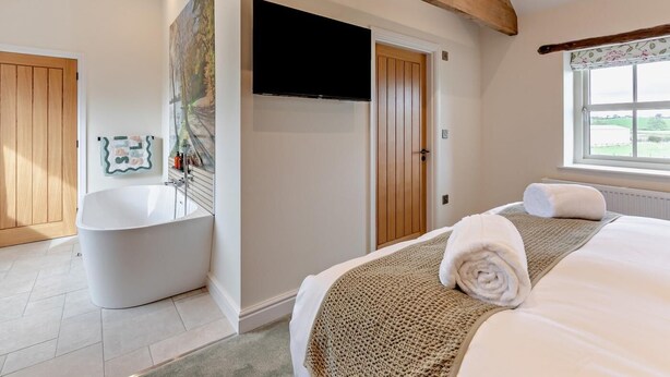 A bedroom with a large bed, a bathtub, a television, and a window with a view. - 2 Bed in Carlisle (oc-96302) (Scaleby)