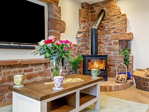 En stenkamin med en tv monterad ovanför, ett träbord med en vas med blommor och en korg med ved.