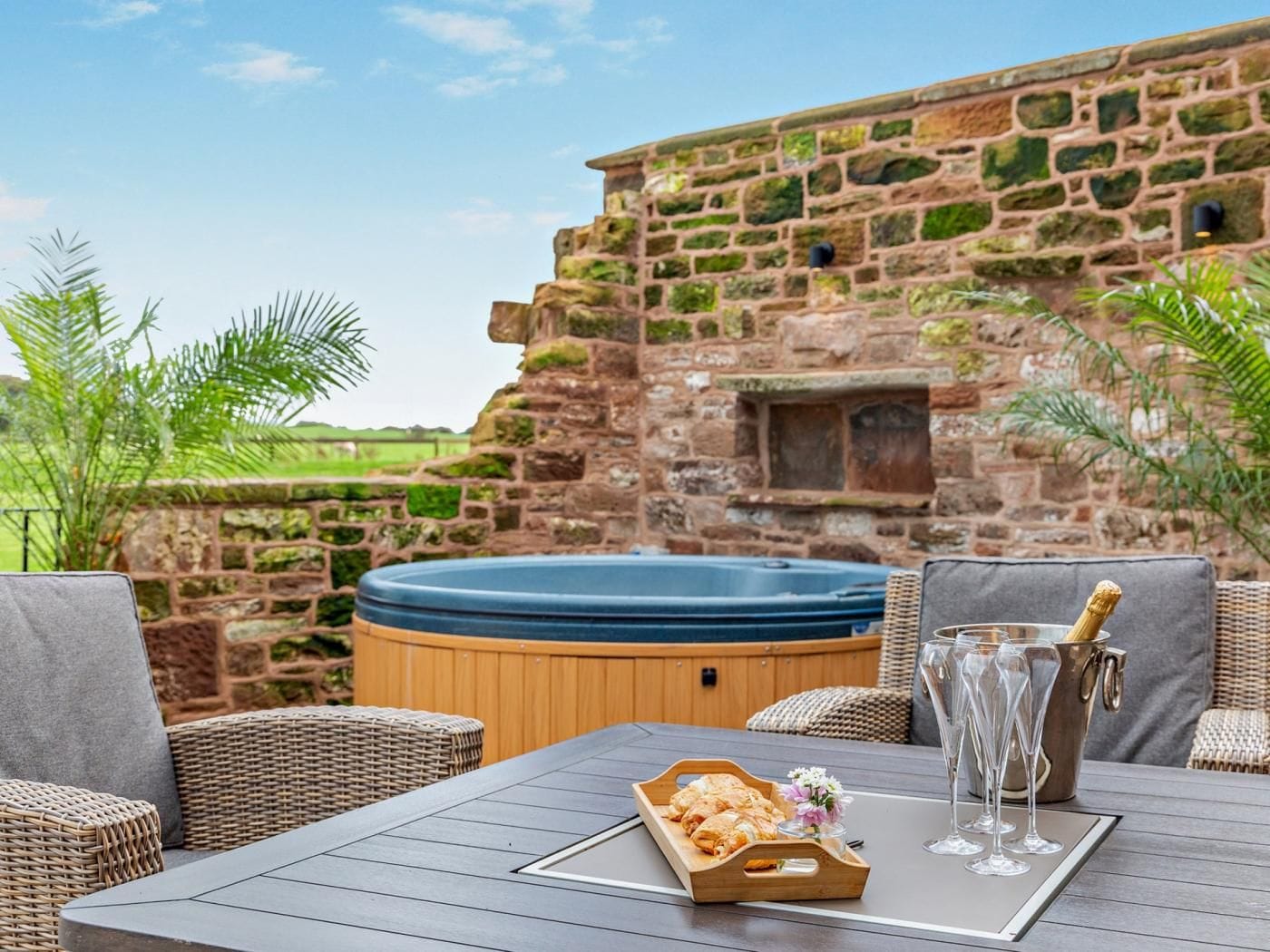 A hot tub, wicker furniture, and a table with a tray of pastries and glasses.