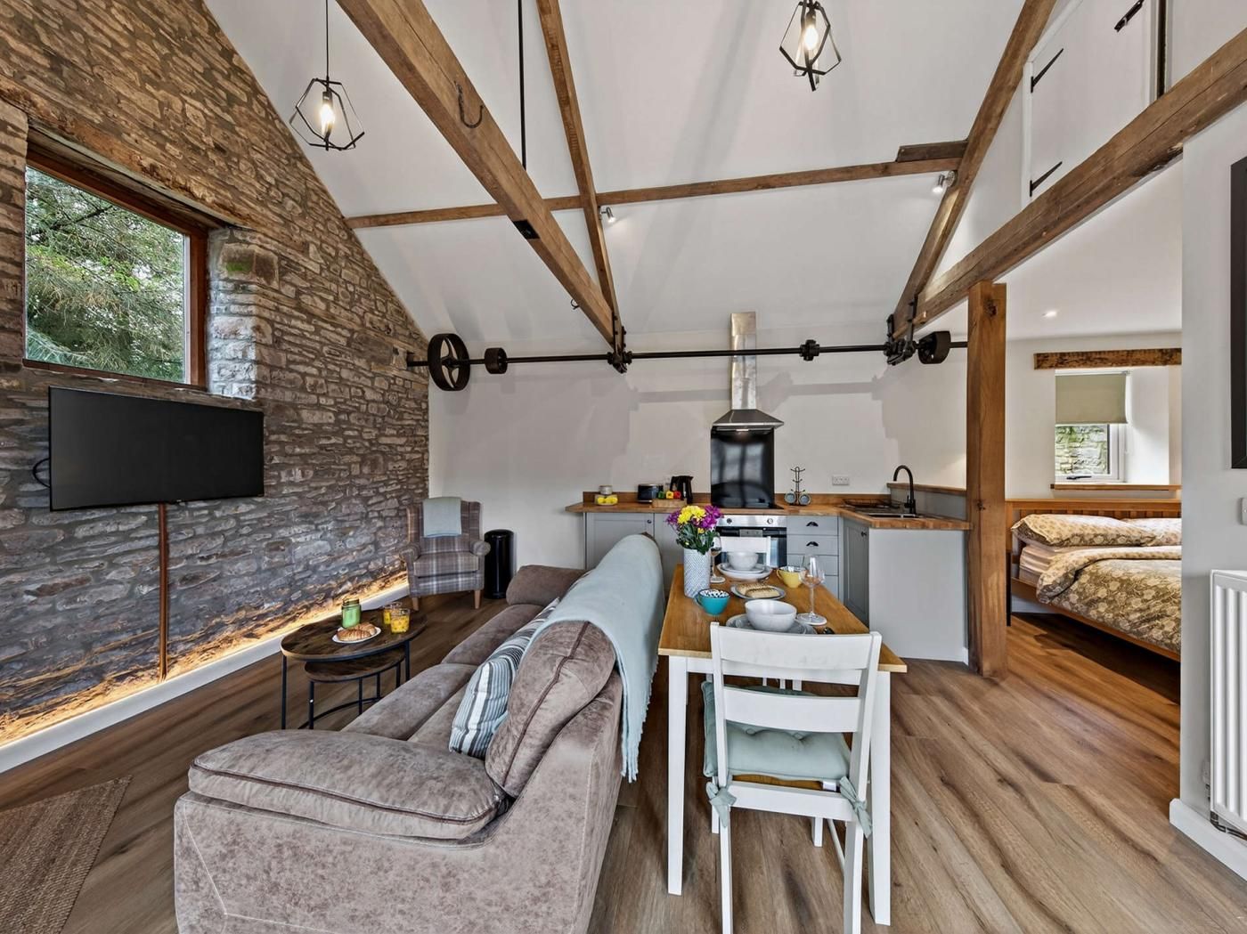 A cozy interior with a stone wall, wooden beams, a dining area, and a kitchenette.