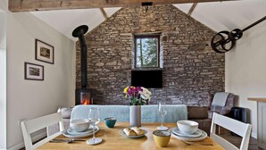A dining area with a stone wall, wooden beams, a fireplace, and a table set with plates, glasses, and flowers. - 1 Bed in Brecon (oc-96359) (Cantref)