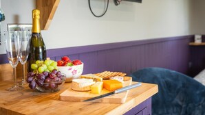 Una mesa de madera con una botella de vino, copas, uvas, fresas, queso y galletas.