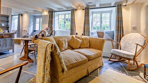 Ein gemütliches Zimmer mit einer Couch, einem Schaukelstuhl, einem Esstisch mit Stühlen und einer Küchenzeile.