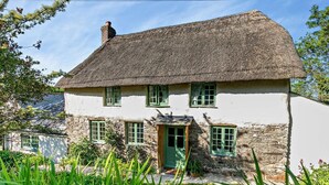 Ein traditionelles Haus mit einem Strohdach, Steinuntergrund, grünen Fenstern und einer kleinen Veranda.