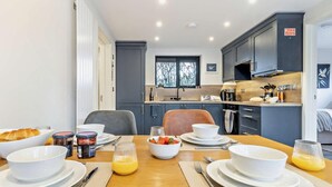 Una cocina moderna con armarios oscuros, una mesa de comedor lista con platos, tazones y cubiertos, y un ventanal con vistas al exterior.