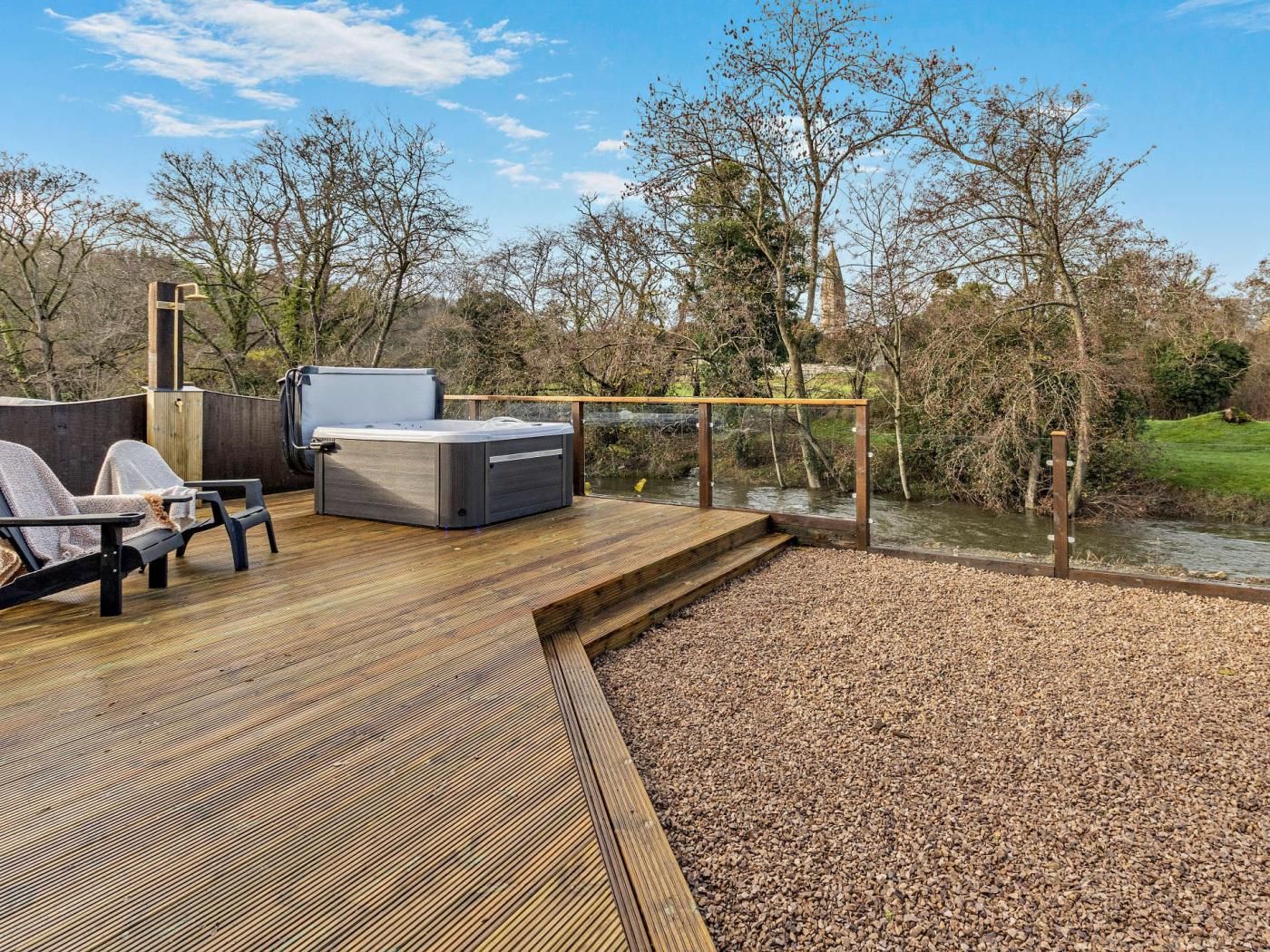 A wooden deck with outdoor seating and a hot tub, overlooking a river.