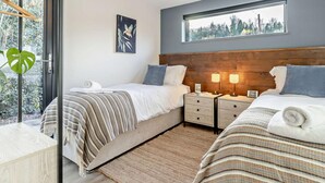 Un dormitorio moderno con dos camas, un ventanal y vistas a árboles.