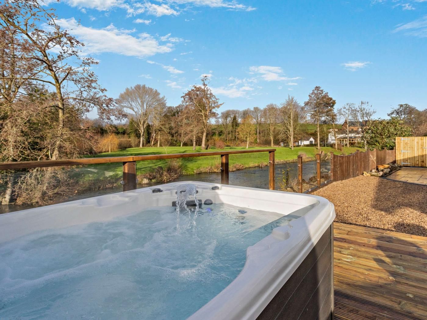 A hot tub on a wooden deck with a view of a river and trees.