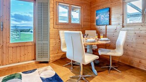 A wooden cabin interior with a dining table, white chairs, a TV, and a large window with a view. - 2 Bed in Middlesbrough (oc-96344) (Skutterskelfe)