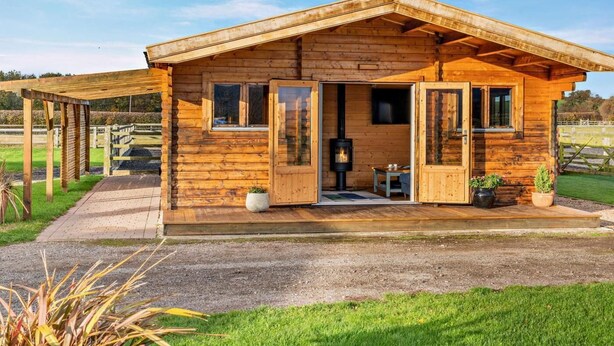 A wooden cabin with a porch, a fireplace, and a small table. - 2 Bed in Middlesbrough (oc-96344) (Skutterskelfe)