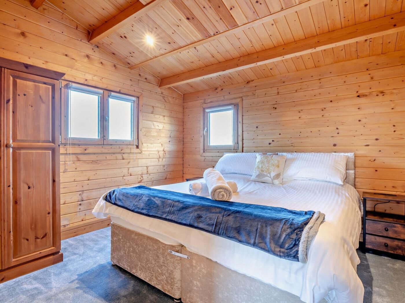 A wooden-paneled bedroom with a bed, two windows, and a wardrobe.