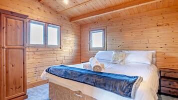 A wooden-paneled bedroom with a bed, two windows, and a wardrobe.