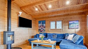 A cozy cabin interior with a wood-burning stove, a blue sofa, a wooden ceiling, and two windows. - 2 Bed in Middlesbrough (oc-96344) (Skutterskelfe)