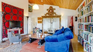 Ein Wohnzimmer mit Holzboden, einer roten Wand mit Muster, einem blauen Sofa, einem Couchtisch, einem Kamin und einem Bücherregal.