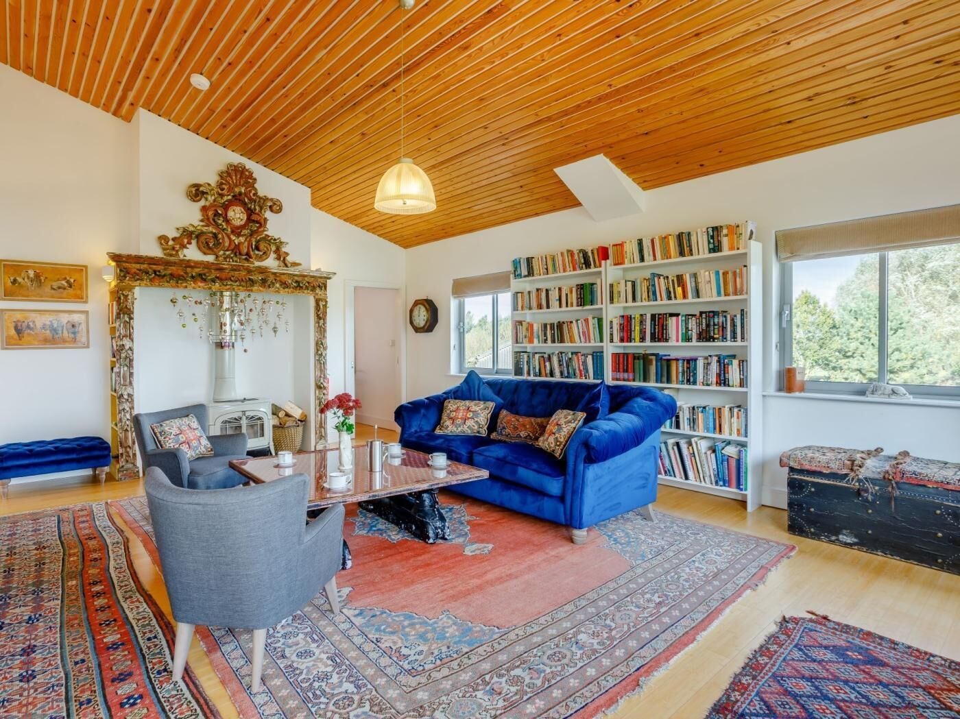 A living room with a blue sofa, a coffee table, a bookshelf, and a large window.