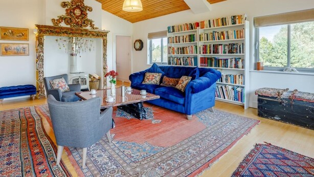 Ein Wohnzimmer mit einem blauen Sofa, einem Couchtisch, einem Bücherregal und einem großen Fenster.