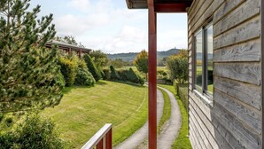 Eine Holzhütte mit Veranda, die auf eine gepflegte Rasenfläche und eine ferne Hügellandschaft blickt.