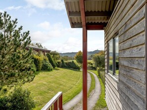 A wooden cabin with a porch overlooking a well-maintained lawn and a distant view of hills. - 2 Bed in Glastonbury (oc-79499) (Lower Godney)