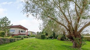Ein Wohnhaus mit gepflegtem Rasen, einem großen Baum und einem Gebäude mit rotem Dach und weißen Wänden.