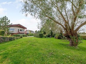 A residential property with a well-maintained lawn, a large tree, and a house with a red roof and white walls. - 2 Bed in Glastonbury (oc-79499) (Lower Godney)