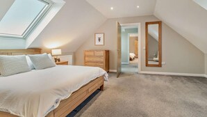 Ein Schlafzimmer mit Dachfenster, einem Bett, einer Kommode, einem Spiegel und einer Tür zu einem weiteren Raum.