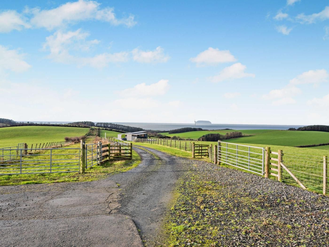 A rural landscape with a gravel path leading to a fenced area with a building.