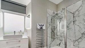 Ein modernes Badezimmer mit einer Marmordusche, einem weißen Waschtisch mit Fenster und einem Handtuchhalter mit Handtuch.