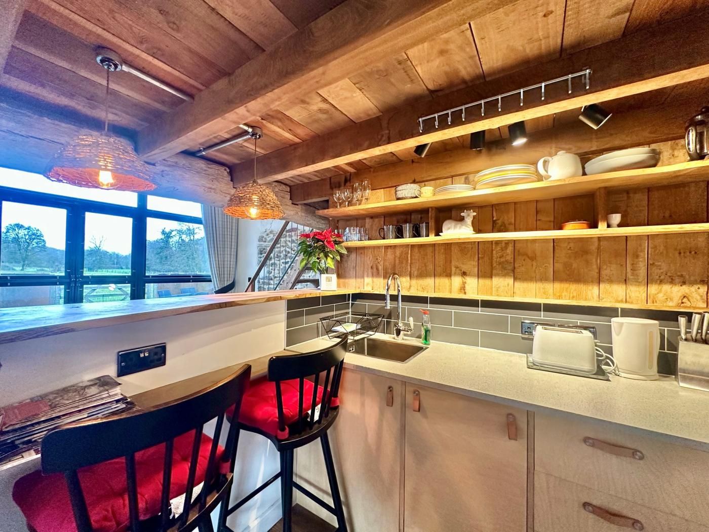 Una cocina moderna con vigas de madera, un ventanal grande y un comedor con sillas rojas.