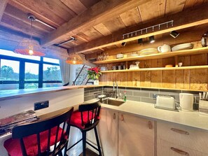 A modern kitchen with wooden beams, a large window, and a dining area with red chairs. - 1 Bed in Tiverton (oc-96405) (Washfield)